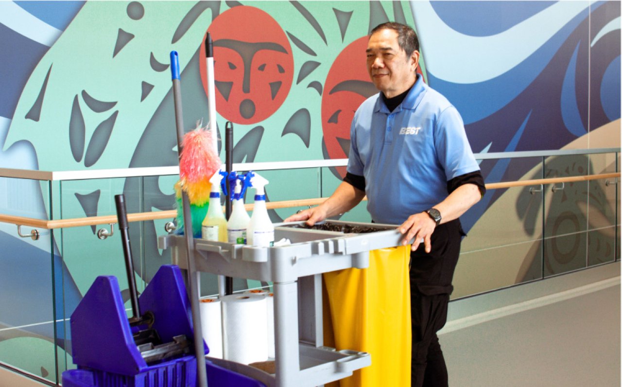Janitorial worker moving a cleaning cart through a facility.